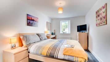 A bedroom with a bed, bedside table, lamp, TV, and artwork.
