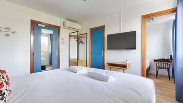 Una camera d'albergo con un letto grande, una scrivania, una sedia, una televisione e un bagno visibile attraverso una porta aperta.