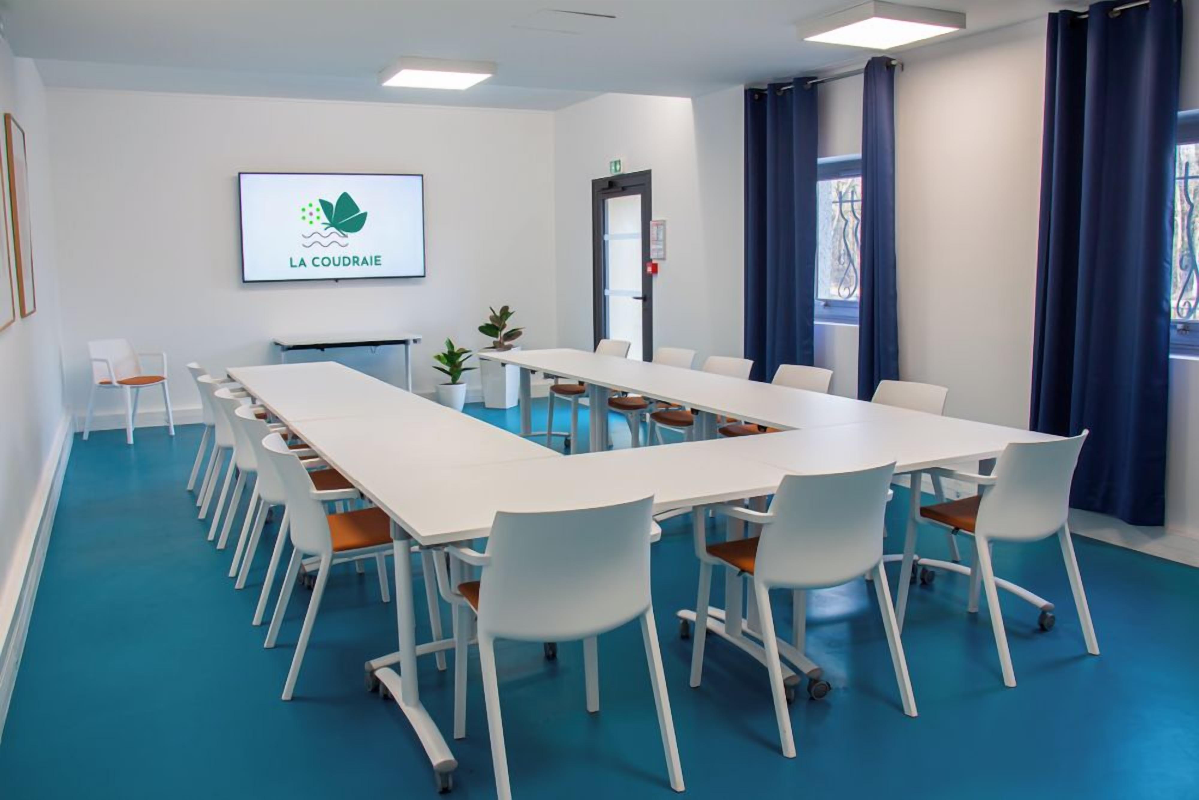 Ein Konferenzraum mit einem langen Tisch, weißen Stühlen und einem Logo an der Wand.