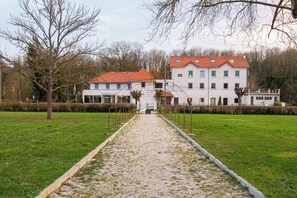 A pathway leading to a building with a red roof and multiple windows, surrounded by trees and a grassy area. - Domaine De La Coudraie (Versigny)