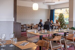 Restaurante com mesas postas para refeições, uma árvore de Natal e uma parede estampada.