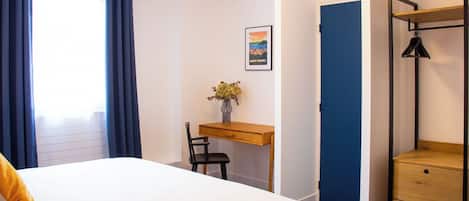 A bedroom with a bed, a desk, a chair, a shelf, and a door.