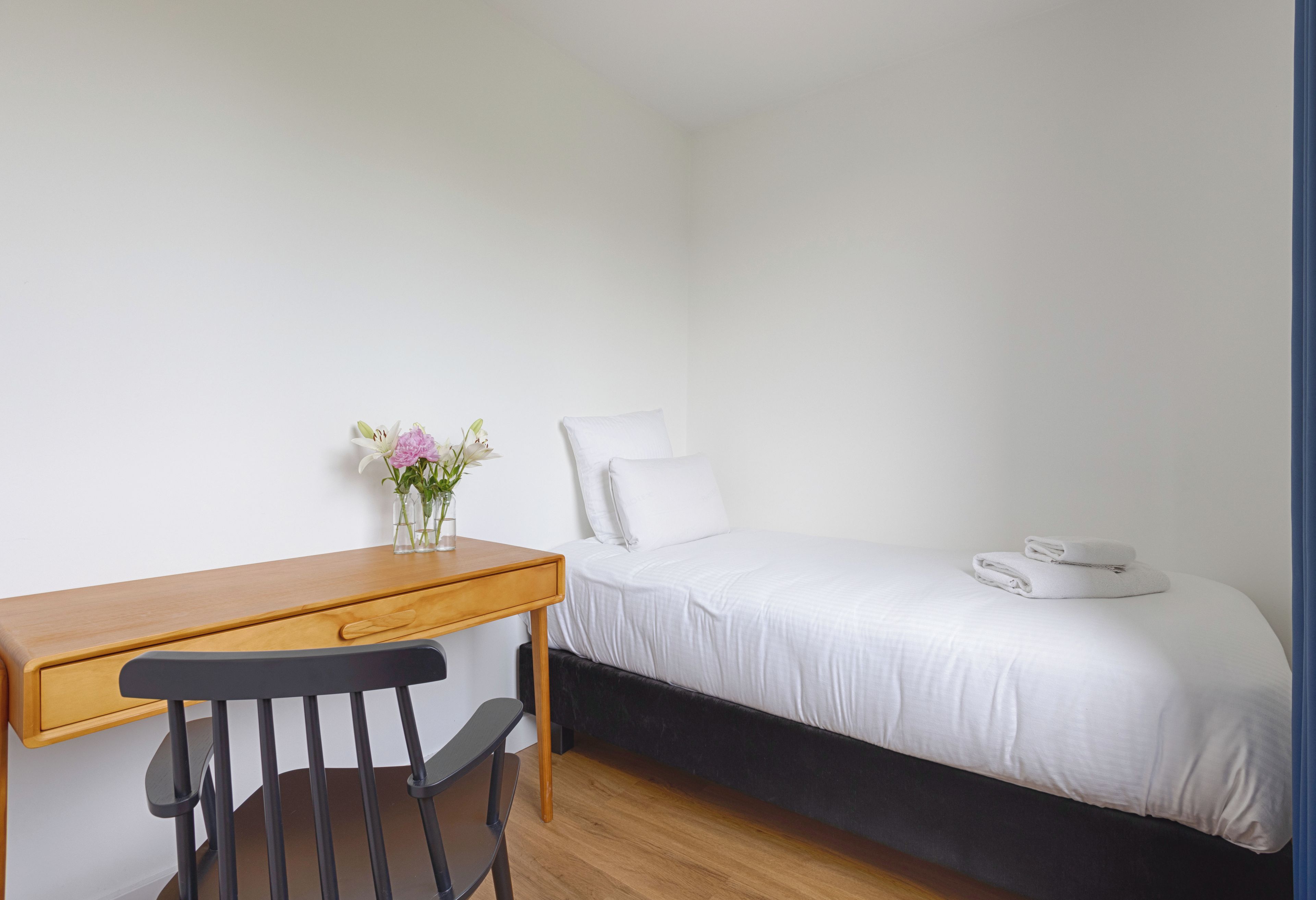 Una habitación pequeña y limpia con una cama individual, un escritorio de madera y una silla.