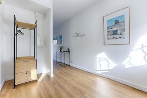Quarto com piso de madeira, guarda-roupa de estrutura metálica, uma mesinha com uma planta e um quadro na parede.