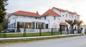 A modern two-story building with a white facade, red-tiled roofs, and a black metal fence in front. - Domaine De La Coudraie (Versigny)