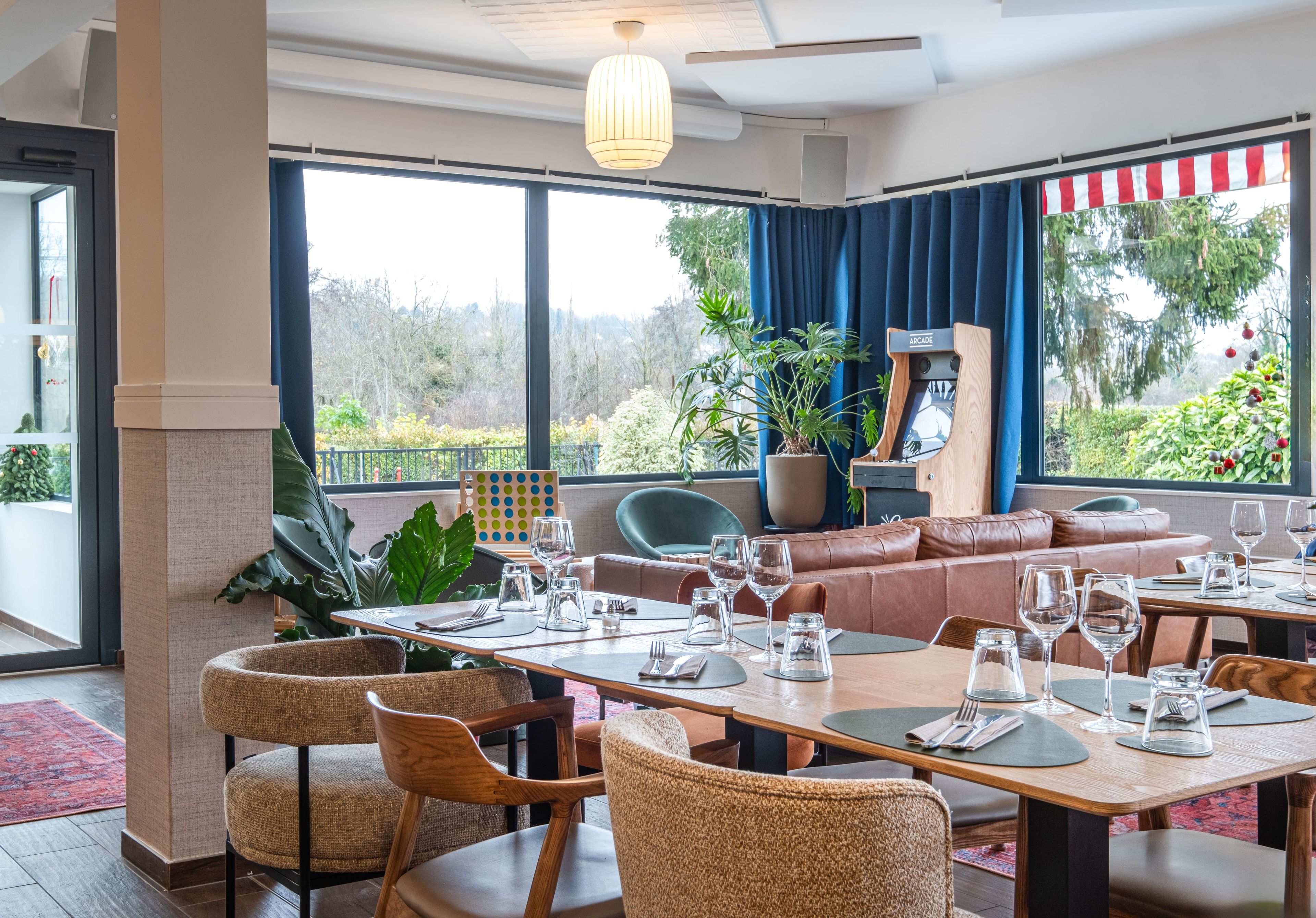 Un ristorante con un lungo tavolo imbandito per un pasto, circondato da sedie. È presente un'ampia finestra con vista sul verde circostante.