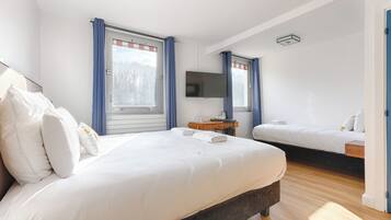 Camera d'albergo con un letto grande, un letto più piccolo, una scrivania, una televisione a schermo piatto e una finestra con tende.