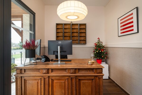 A reception desk with a computer monitor, a potted plant, a small Christmas tree, and a framed picture on the wall.