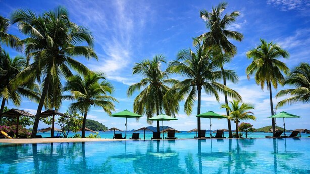A clear blue pool surrounded by palm trees and umbrellas, with a view of the sea in the background. - Peridot By The Sea At Redang (Redang Island)