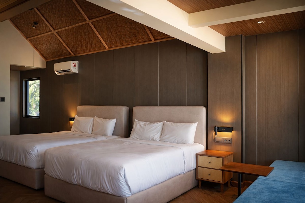 A modern hotel room with two beds, a wooden ceiling, and a small table.