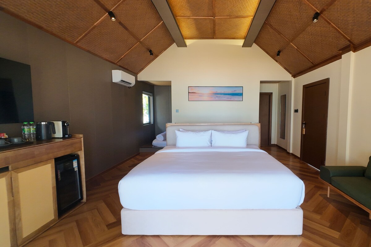 Un dormitorio amplio con una cama grande, techo de madera, una kitchenette pequeña y un sofá verde.