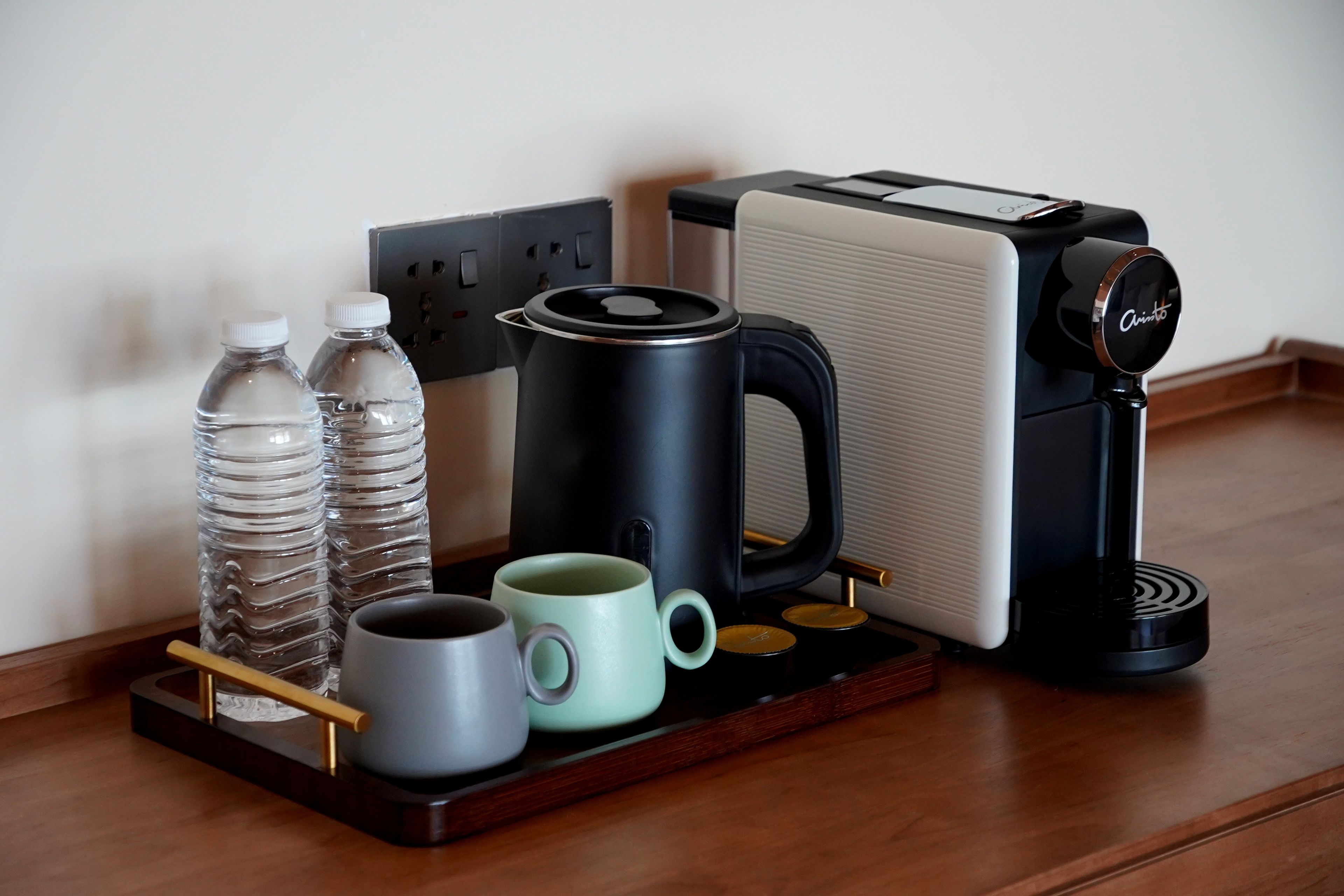 A coffee maker, two water bottles, and two mugs on a tray.