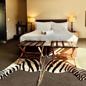 A hotel room with a bed, two bedside lamps, a small table, and a zebra-patterned rug. - Blix Inn (Stellenbosch)