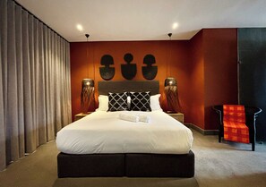 A modern hotel room with a large bed, dark headboard, two bedside tables, and a red chair. - Blix Inn (Stellenbosch)