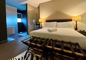 A hotel room with a bed, two bedside lamps, a nightstand, and a view of a bathroom. - Blix Inn (Stellenbosch)