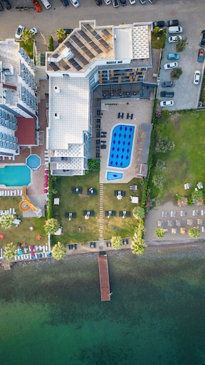 Vista aérea de un hotel con piscina, mobiliario exterior y un muelle que se adentra en el agua.