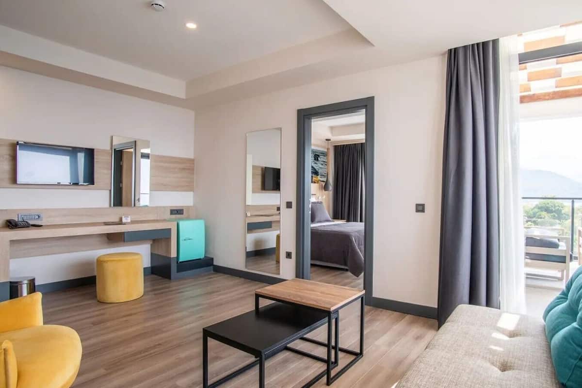 Una habitación de hotel moderna con cama, escritorio, televisor, kitchenette pequeño y balcón con vistas.
