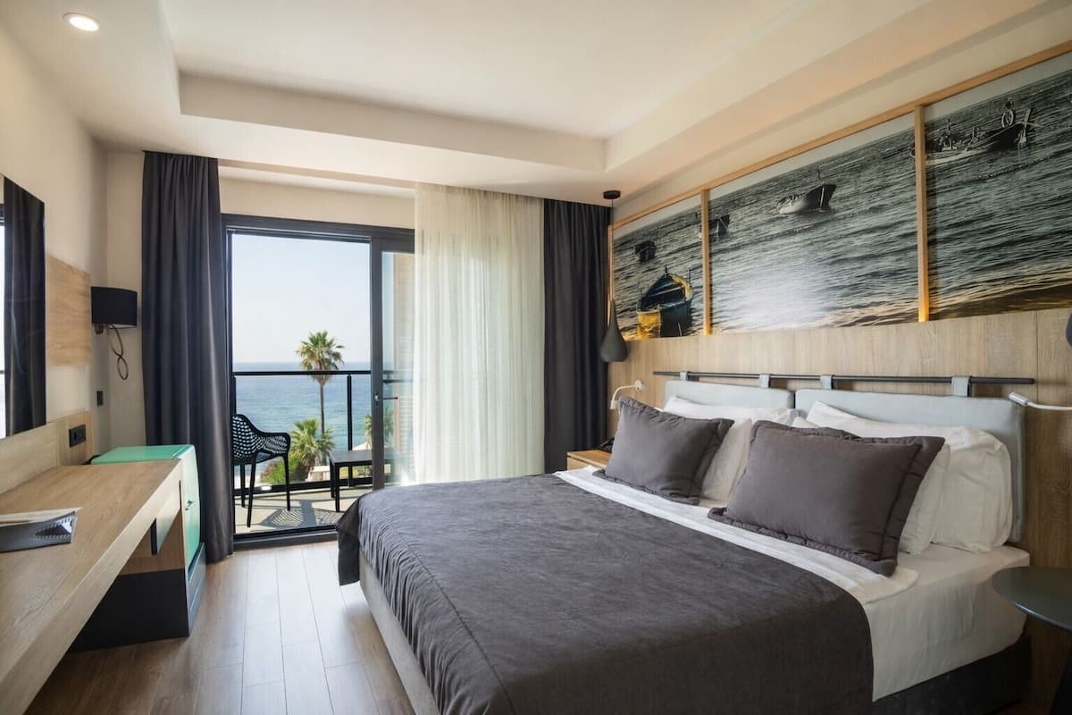 Habitación de hotel con una cama grande, un escritorio, una silla, un balcón con vistas al mar y un cuadro en la pared.