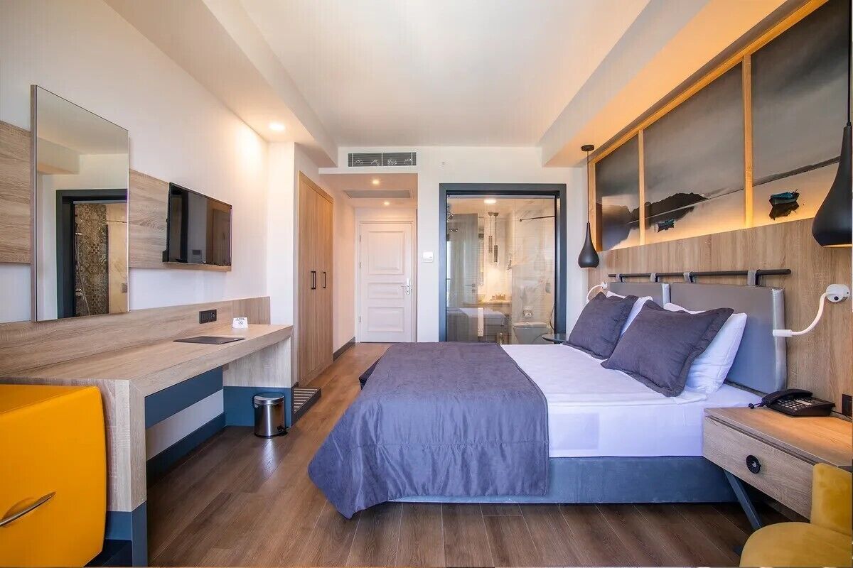 A modern hotel room with a bed, bedside table, mirror, and a view of the bathroom.
