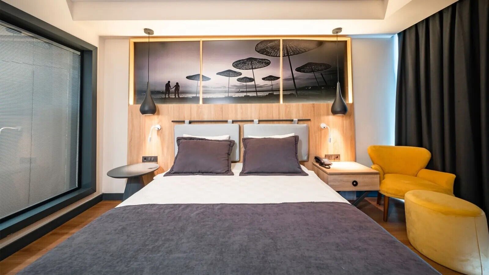A modern hotel room with a large bed, a nightstand, a chair, and a wall-mounted artwork.