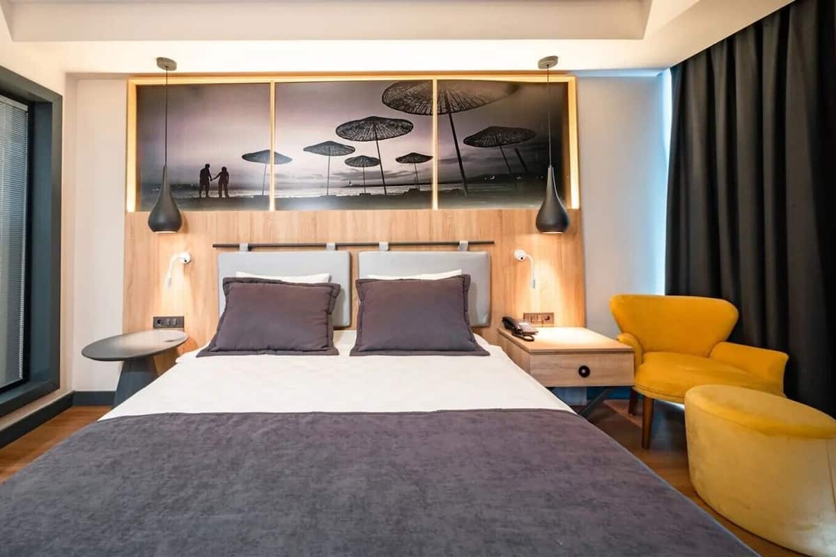 Una habitación de hotel moderna con una cama grande, una mesita de noche, una silla y una obra de arte colgada en la pared.