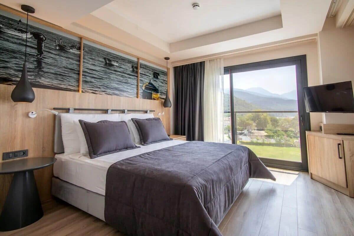 Una habitación de hotel moderna con una cama grande, un televisor, vistas a las montañas y un cuadro en la pared.