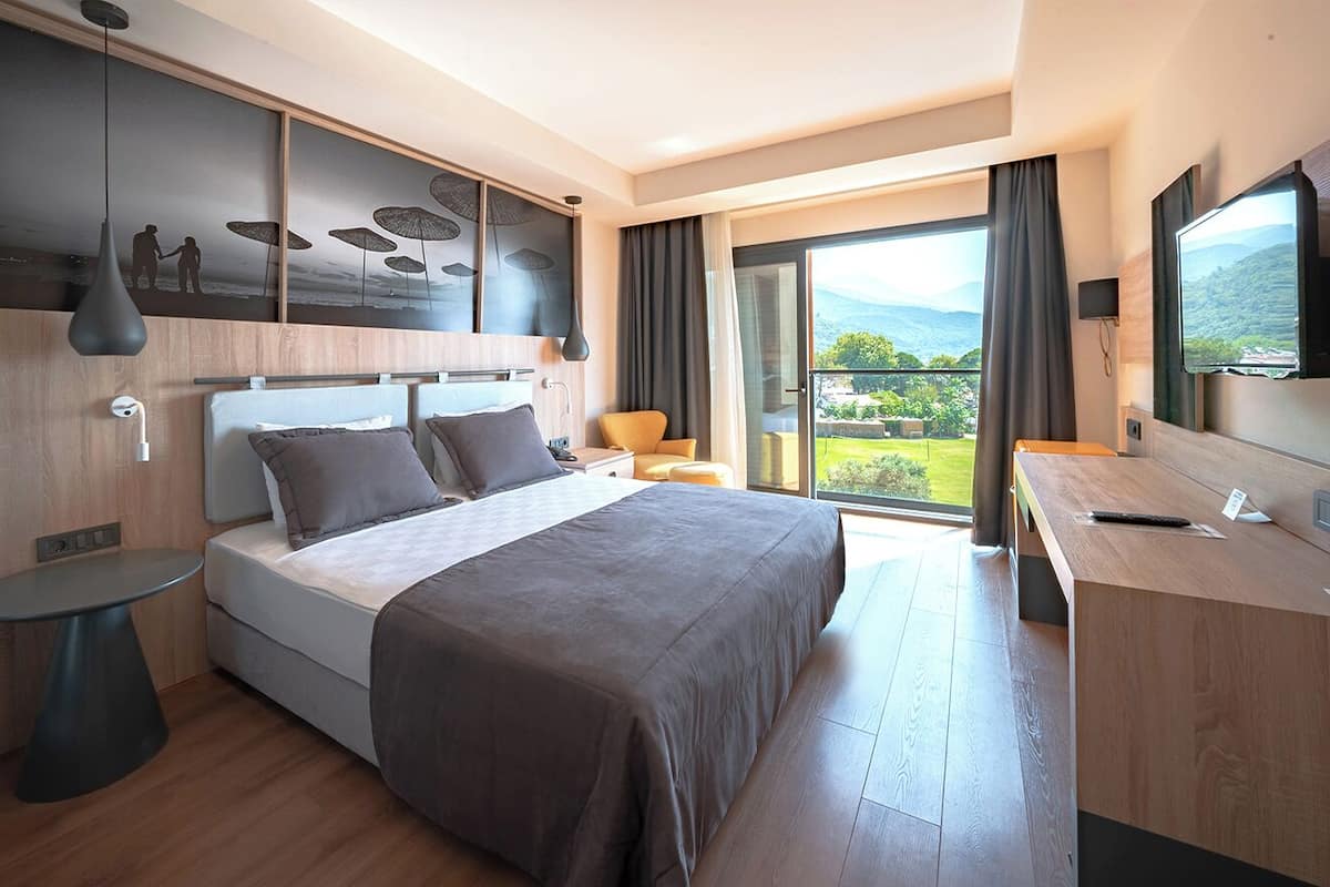 Una habitación de hotel moderna con una cama grande, un escritorio, una silla, un televisor y un balcón con vistas a la montaña.