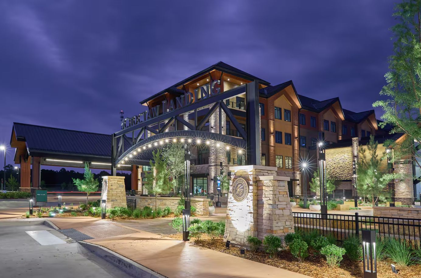 A hotel entrance with a large archway, stone pillars, and well-lit pathways.
