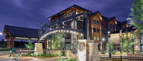A hotel entrance with a large archway, stone pillars, and well-lit pathways.