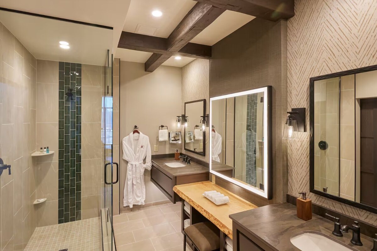 A modern bathroom with a glass shower enclosure, a vanity with a large mirror, and a robe hanging on a rack.