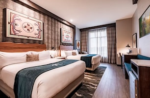 Una habitación de hotel con dos camas, un escritorio y obras de arte en las paredes.