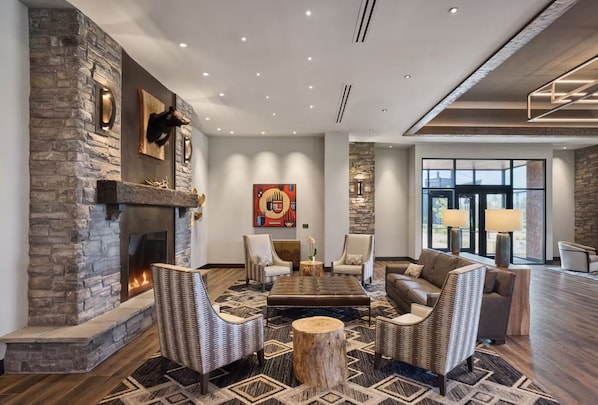 A spacious living area with a stone fireplace, comfortable seating, and a large window providing a view. - Choctaw Landing Casino & Resort, Trademark Coll (Broken Bow)