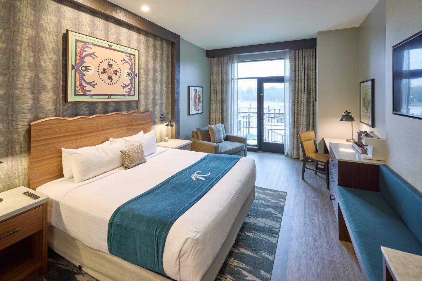 A hotel room with a large bed, a desk, a chair, and a balcony view.