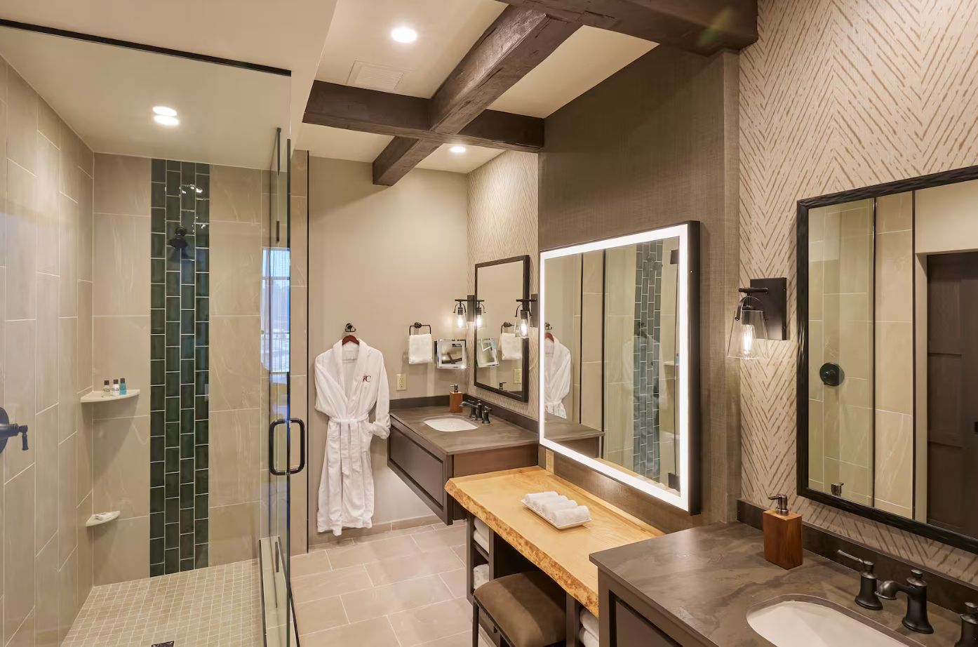 A modern bathroom with a glass shower enclosure, a vanity with a large mirror, and a robe hanging on a rack.