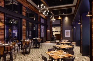 Interior de restaurante con paredes de madera, lámparas colgantes y suelo estampado. Las mesas están preparadas con platos y vasos.