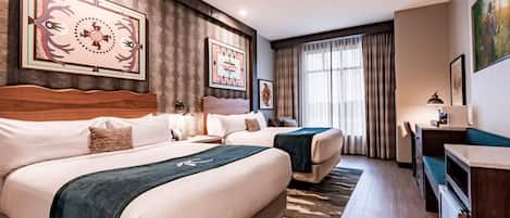A hotel room with two beds, a desk, and artwork on the walls.