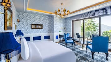 Habitación de hotel con cama, sillas azules, un escritorio y vistas al exterior.