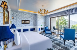 Hotellihuone, jossa on sänky, siniset tuolit, työpöytä ja näkymä ulos.