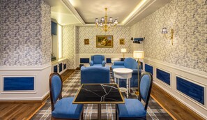 A room with a checkered floor, blue upholstered chairs, a black marble table, and patterned wallpaper.
