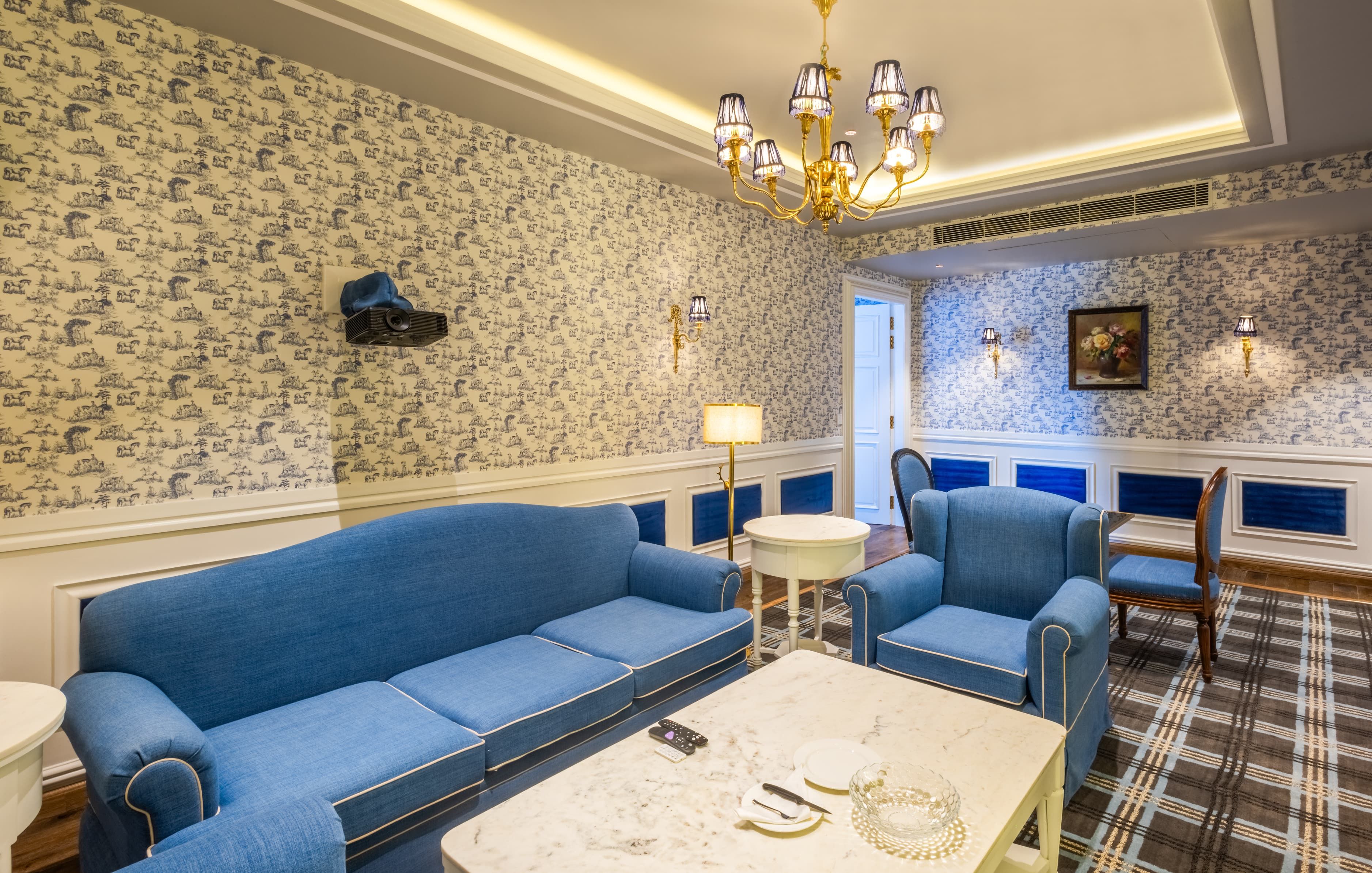 Una stanza con un divano blu, una poltrona abbinata, un tavolino da caffè in marmo e carta da parati decorata.
