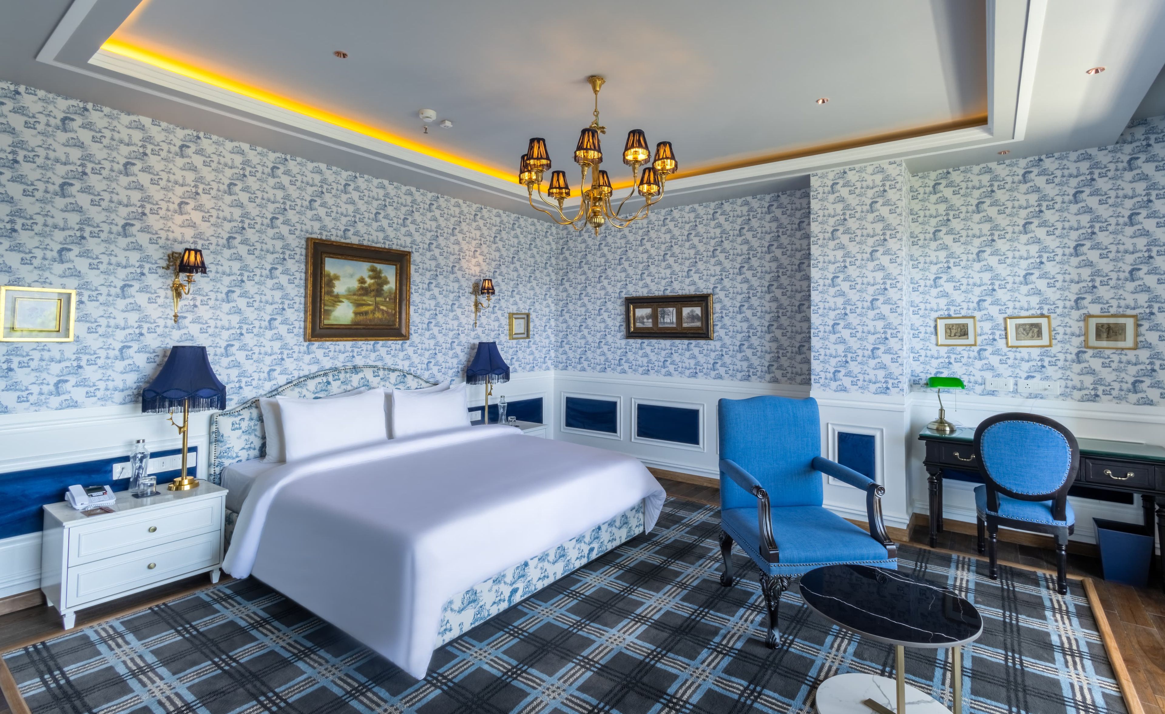Un dormitorio con una cama, un sillón azul, un escritorio y una araña.