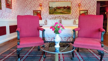 Una stanza con un letto, due sedie, un tavolo con un vaso di fiori e carta da parati decorata.