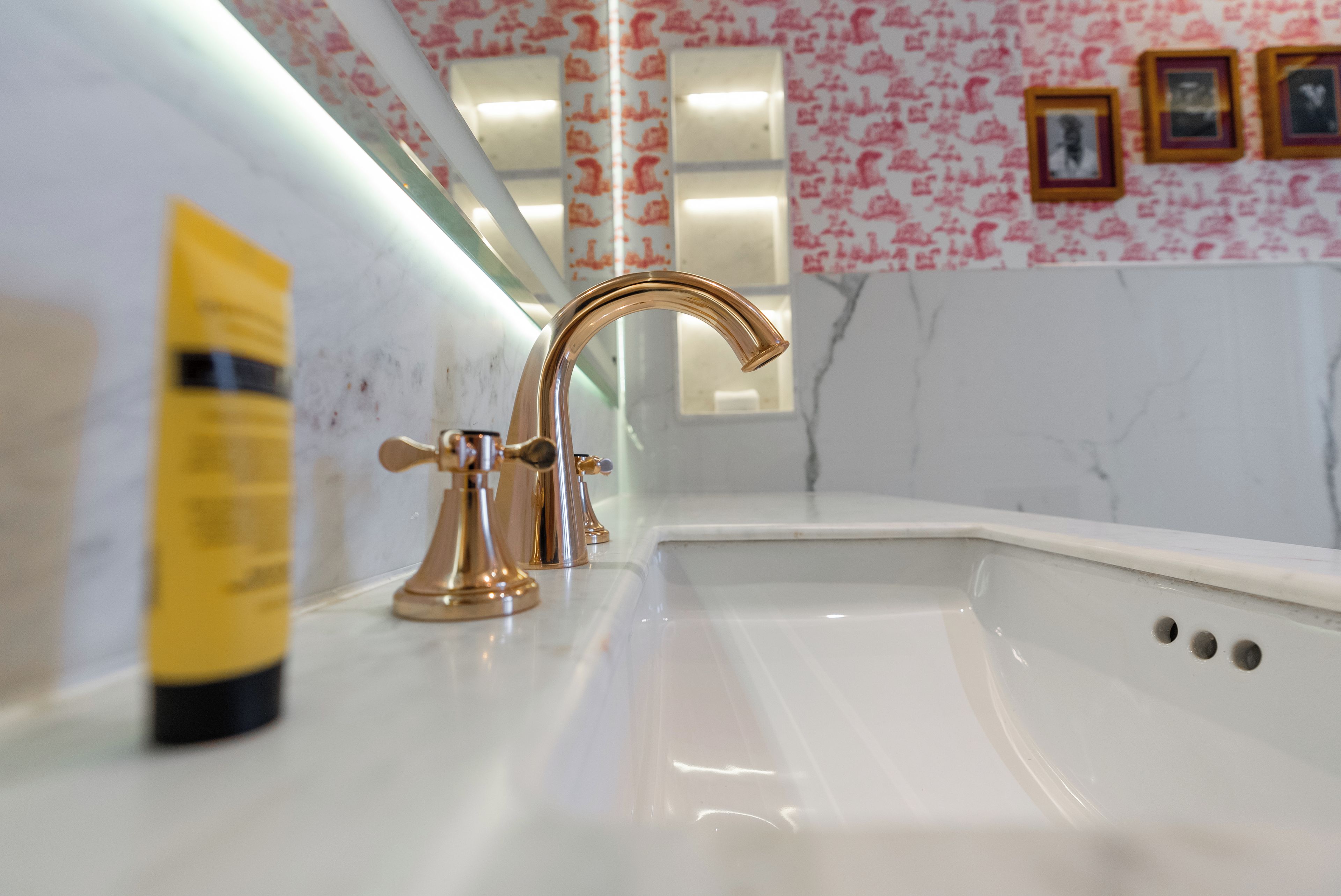 Un baño con un lavamanos blanco, un grifo dorado y una botella amarilla sobre el mostrador.