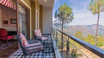 A balcony with wicker chairs and a small table, overlooking a mountainous landscape.