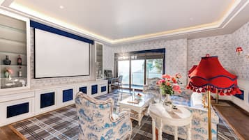 A spacious living room with a large screen, comfortable seating, and a red lamp.