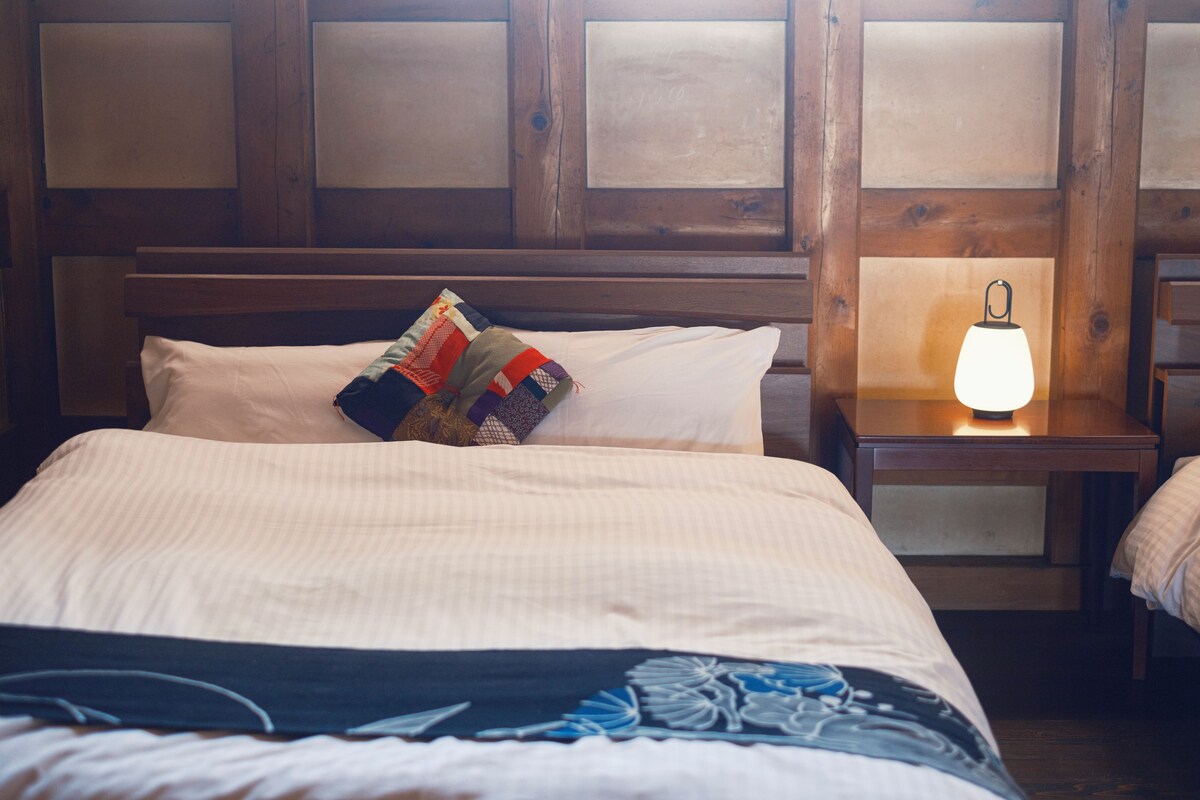 A neatly made bed with a patterned pillow, a bedside lamp, and a wooden headboard.