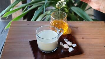 A wooden table with a glass cup of milk, a honey jar, and a honey dipper.
