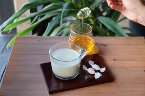 A wooden table with a glass cup of milk, a honey jar, and a honey dipper.