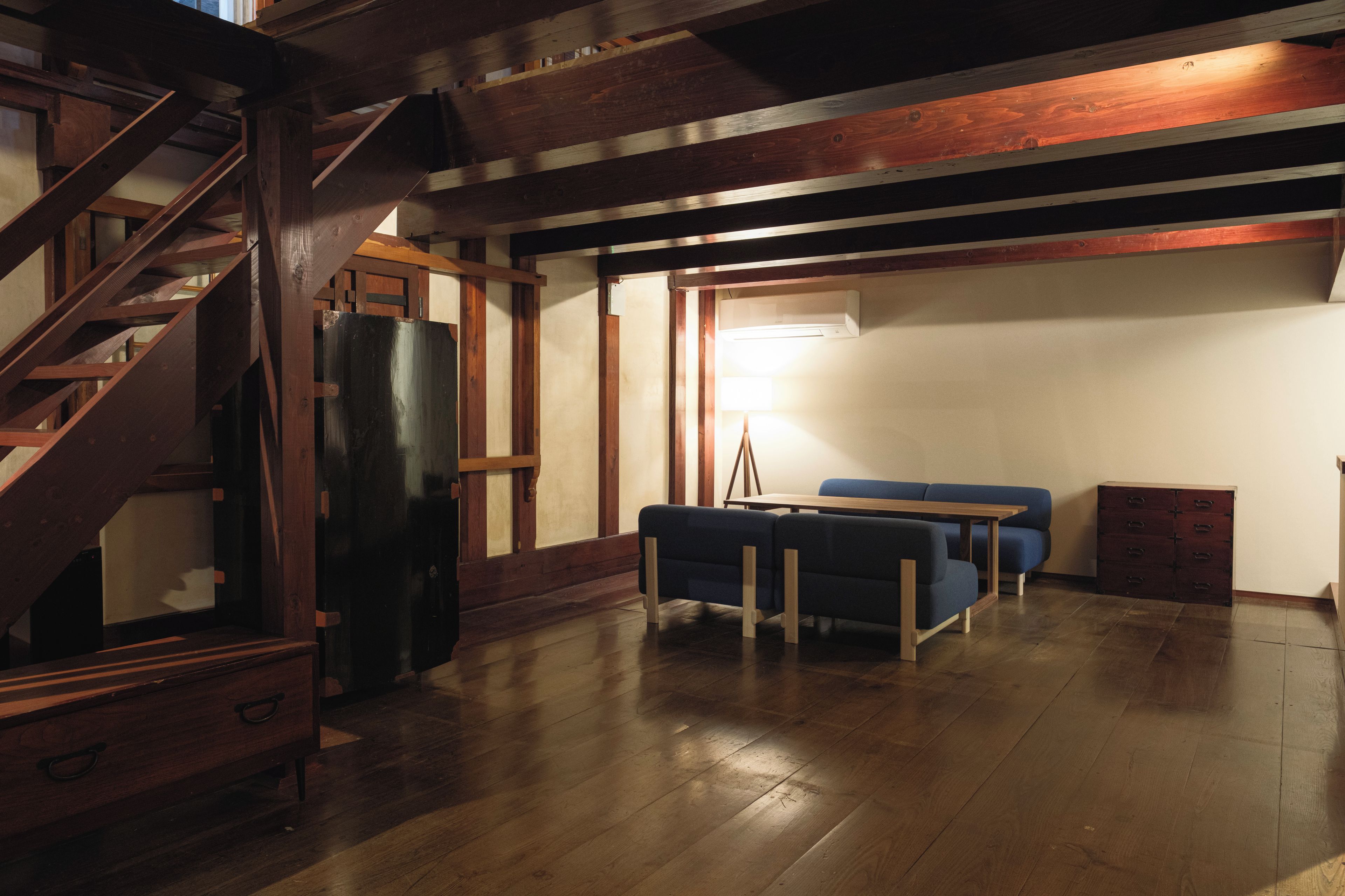 Un'ampia stanza con una scala in legno, un divano blu e un tavolo in legno.