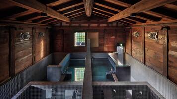 A wooden cabin with two separate bathing areas, each with a small window and a fan.